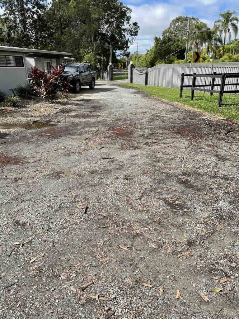 Poorly constructed driveway with uneven, contaminated road base and visible patches of clay and organic matter, lacking proper compaction.