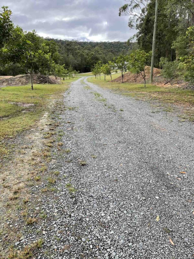Driveway with loosely spread gravel and no defined edges, lacking compaction, grading, and structural integrity for long-term durability.
